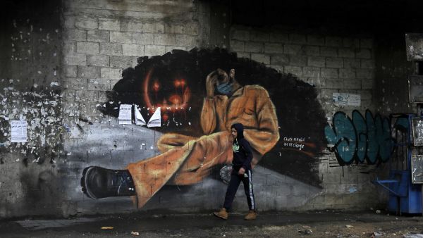A young boy walks past a mural painting with writing in Arabic that reads "we are tired" near Al-Nour square in the northern city of Tripoli, following overnight clashes between security forces and anti-government protesters, on January 29, 2021. JOSEPH EID / AFP
