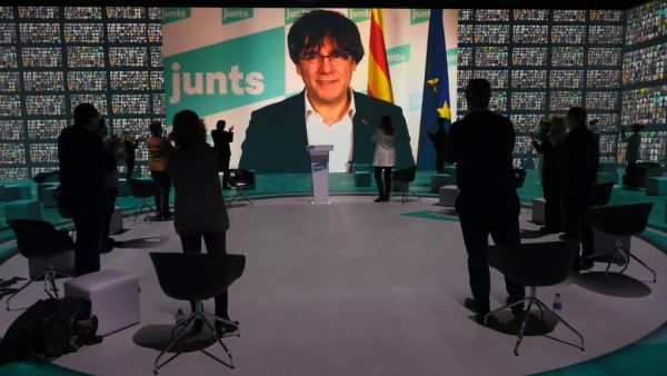 Attendees applaud as a screen displays images of former Catalan president Carles Puigdemont during "Junts per Catalunya" party (Together For Catalonia) closing campaign meeting for the up-coming Catalonia regional elections in Barcelona on February 12, 2021. More than three years after a failed bid to break away from Spain, Catalonia goes to the polls on February 14, 2021 for an election that Madrid hopes will unseat the region's ruling separatists.  LLUIS GENE / AFP