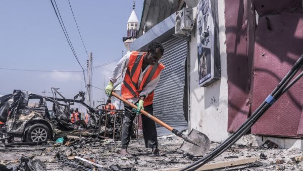 A rescue worker clears debris with a shovel at the site of a suicide car bombing attack near a security checkpoint in Mogadishu on February 13, 2021. Three people were killed and eight wounded after a car bomb detonated near a security checkpoint in the Somali capital Mogadishu, a security official and witnesses said. Abdirazak Hussein FARAH / AFP