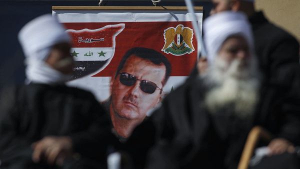 Members of the Druze community sit near a billboard bearing the portrait of Syrian President Bashar Assad during a rally in the village of Majdal Shams in the Israeli-annexed Golan Heights on February 14, 2021, to protest the 1981 Israeli annexation law of the strategic plateau which the Jewish state captured from Syria during the 1967 Arab-Israeli war. JALAA MAREY / AFP