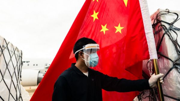 A man wearing a face mask holds the Chinese national flag as he looks on while workers offload an Air Zimbabwe aeroplane with a donation of 200,000 doses of the Sinopharm coronavirus vaccine from China on February 15, 2021 at the Robert Mugabe International Airport. Jekesai NJIKIZANA / AFP