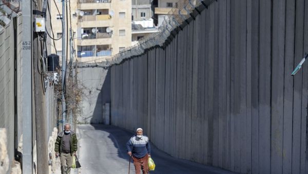 Palestinian men walk by Israel's controversial barrier separating the West Bank city of Abu Dis (background) and East Jerusalem (foreground), on February 16, 2021. AHMAD GHARABLI / AFP Palestinian men walk by Israel's controversial barrier separating the West Bank city of Abu Dis (background) and East Jerusalem (foreground), on February 16, 2021. AHMAD GHARABLI / AFP