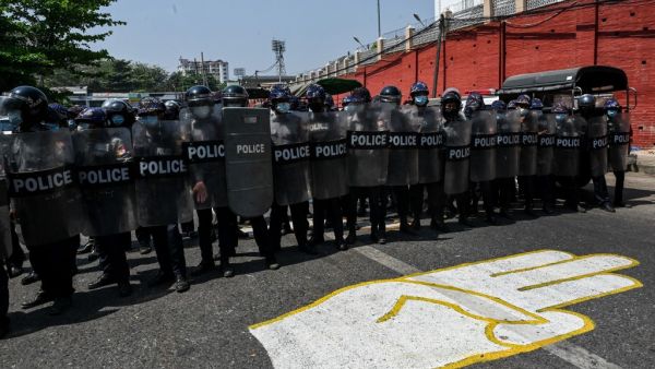 Riot police stand guard on a road, behind a street mural of the protesters' three finger salute, after a clash between pro-junta supporters and anti-military coup protesters in Yangon on February 25, 2021. Ye Aung Thu / AFP