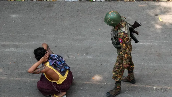 A soldier stands next to a detained man 