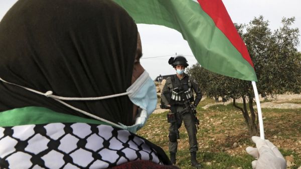 A Palestinian woman waves the national flag at an Israeli border guard 