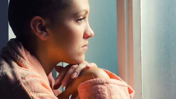 Young depressed cancer patient standing in front of hospital window