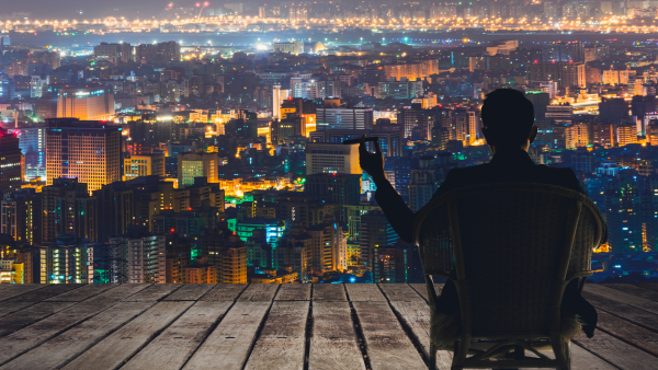 Silhouette of businessman sit on chair and hold a cigar and looking at the city in night