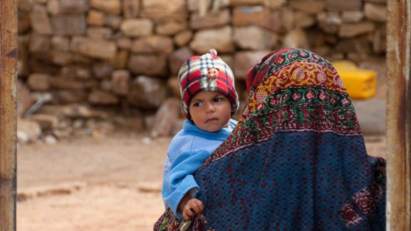 A woman in traditional colorful clothes walks with her little son in her arms