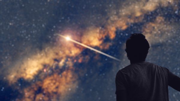 Man observing the night sky and Milky way with a shooting star trail