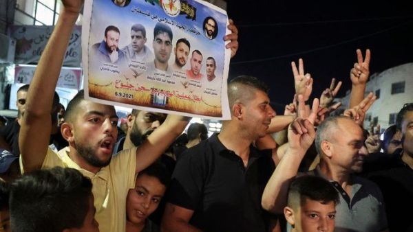 A Palestinian man flashes a poster by the militant group Islamic Jihad of 6 Palestinians who escaped from an Israeli prison, as people celebrate in the Jenin camp in the northern Israeli-occupied West Bank