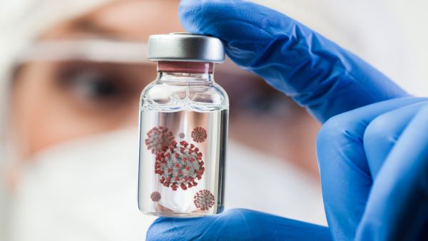 Female UK lab scientist doctor holding glass ampoule vial containing Coronavirus molecule cell
