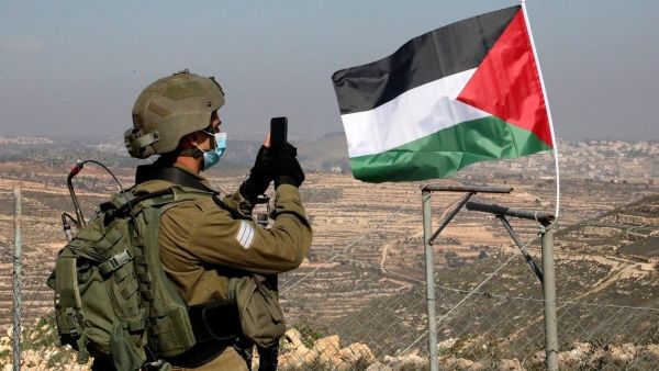 Israeli soldier facing a Palestinian flag