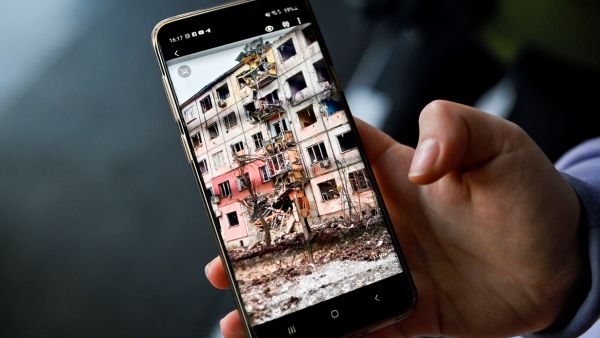 Ukrainian refugee Anna Medianyk shows a photo of her appartment building destroyed by shelling in Kharkiv as she rests in a hotel ballroom, converted into a makeshift refugee shelter in the town of Suceava, on March 15, 2022. (Photo by Armend NIMANI / AFP) Companies, Governments Should Ensure Rights