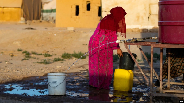 A Syrian woman fills a container with water
