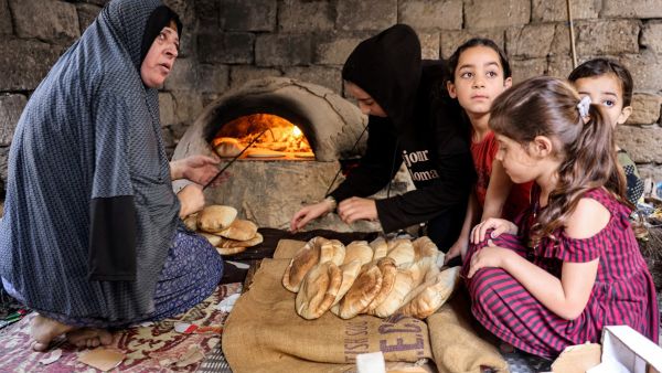 A woman bakes bread in a clay oven next to children in a home in Khan Yunis in the southern Gaza Strip. (Mohammed Abed/ AFP)
