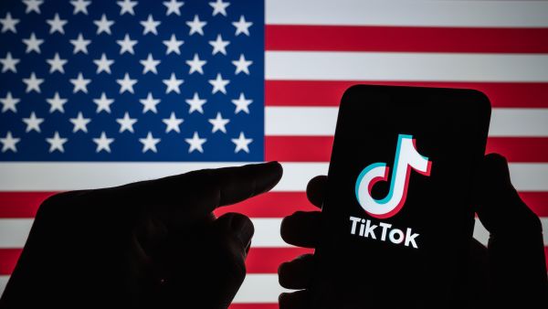 ikTok logo seen on the silhouette of smartphone hold in a hand with blurred American flag on the back (Shutterstock) US congress votes to ban TikTok today, China warns with legal battle on the table