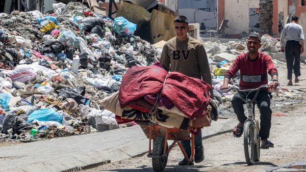 A man walks with a wheelbarrow loaded with blankets and covers past a mound of trash by a destroyed building in the Zaytoun neighbourhood of Gaza City on May 9, 2024. (Photo by AFP) Gaza