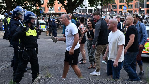 A protester holding a piece of concrete walks towards riot police as clashes erupt in Bristol on August 3, 2024 during the 'Enough is Enough' demonstration held in reaction to the fatal stabbings in Southport on July 29. UK police prepared for planned far-right protests and other demonstrations this weekend, after two nights of unrest in several English towns and cities following a mass stabbing that killed three young girls. (Photo by JUSTIN TALLIS / AFP) UK