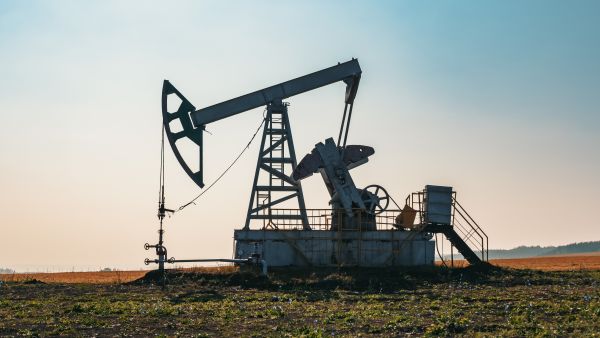 مضخة نفط برية تعمل في حقل مفتوح خلال ساعات النهار، تظهر معدات استخراج النفط الخام وسط أرض زراعية وتحت سماء صافية