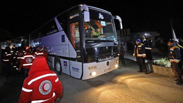 Members of the Syrian Red Crescent and Civil Defence stand by as a convoy of buses carrying rebel fighters and civilians from the Eastern Ghouta enclave town of Harasta arrives in the town of Qalaat al-Madiq, about 45 kilometres northwest of the central city of Hama, early on Mar. 23, 2018. 
(OMAR HAJ KADOUR / AFP)