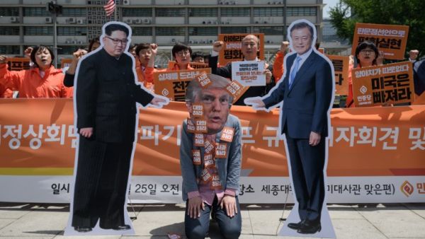 An anti-US protester wearing a face-mask depicting US president Donald Trump (C) kneels between cardboard cutouts of North Korean leader Kim Jong Un (L) and South Korean leader Moon Jae-in (R) (AFP/File Photo)
