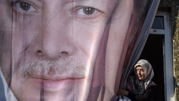 A woman looks from a window partly hidden with a giant poster showing Turkish President Recep Tayyip Erdogan  (AFP)