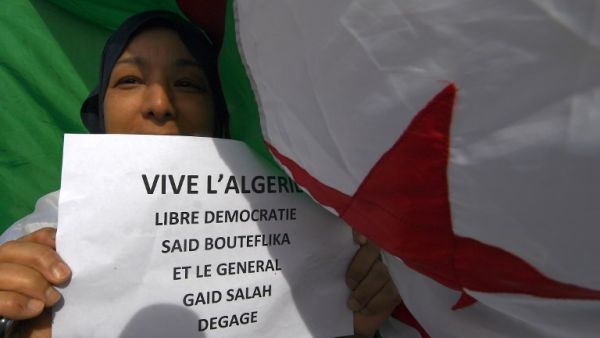 A demonstrator poses with a placard in front of an Algerian flag during a rally in Marseille (AFP)