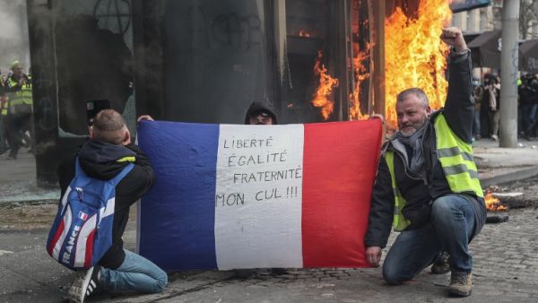 Yellow Vest protesters hold a French national flag reading "Freedom, Equality, Fraternity, my Ass !" as they pose in front of a newsstand set alight during clashes by protesters on the Champs-Elysees in Paris on March 16, 2019. (AFP/ File)