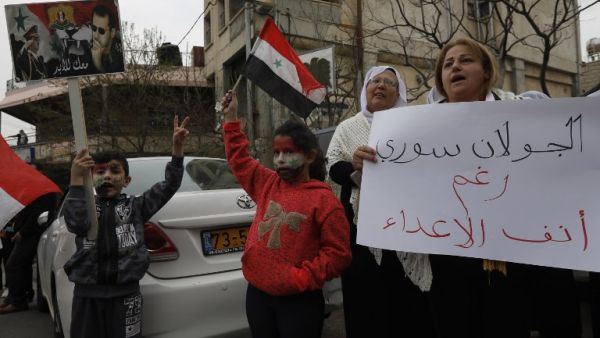 Residents of the Golan Heights raise Syrian flags and a banner with portraits of the Syrian President Bashar al-Assad during a protest against the backing of Israel's capture of the Golan Heights by the US president. (AFP)
