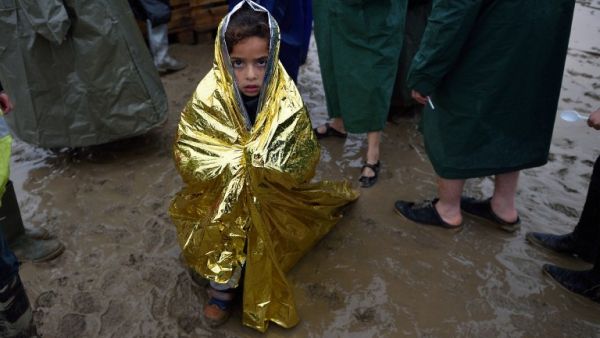 A child wrapped in a survival blanket looks as migrants queue for hot soup on March 13, 2016, in a makeshift camp at the Greek-Macedonian border, near the Greek village of Idomeni, where thousands of refugees and migrants are stranded by the Balkan border blockade. (AFP/Daniel Mihailescu)