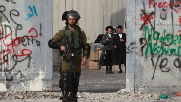 Orthodox Jewish men stand behind Israel's controversial separation barrier as a soldier makes his way through the West Bank entrance to Bethlehem, October 12, 2015. (AFP/File)