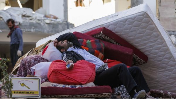 An Iranian man rests as he lies atop salvaged mattresses and items outside damaged buildings in the town of Sarpol-e Zahab near the border with Iraq following a 7.3-magnitude earthquake that left hundreds killed and thousands homeless. 
(ATTA KENARE / AFP)