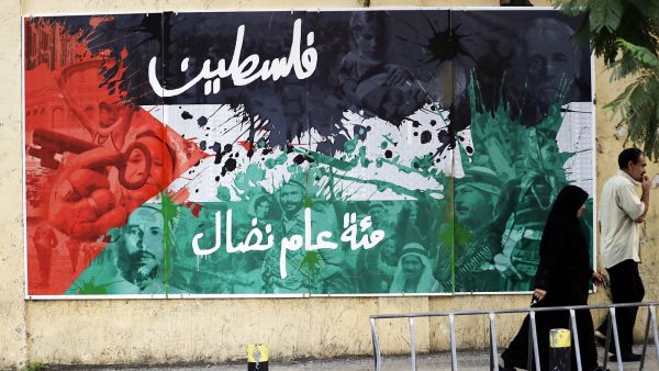 Lebanese people walk past a poster bearing an image of the Palestinian flag and text reading in Arabic: "Palestine, a hundred years of struggle" in Beirut on Dec. 8, 2017 (Joseph Eid/AFP)
