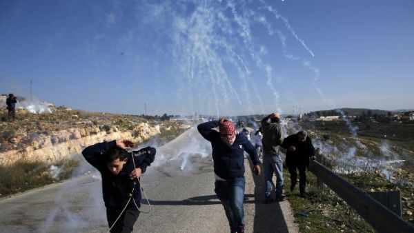 Palestinians run for covers from smoke-grenades during clashes with Israeli security forces following a demonstration in support of Palestinian prisoners on Jan. 13, 2018 (ABBAS MOMANI / AFP)