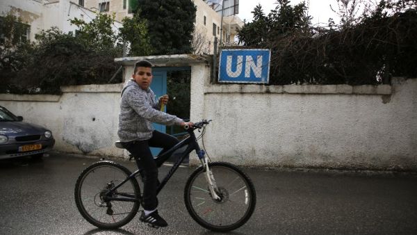 A Palestinian boy cycles past a United Nations' run health center in the Qalandia refugee camp near Ramallah in the West Bank, on Jan. 17, 2018 (ABBAS MOMANI / AFP)