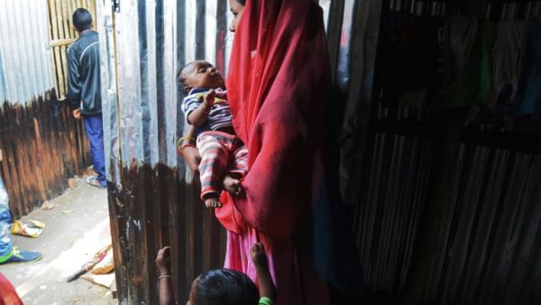 A Rohingya refugee carrying a baby stands at a temporary shelter near the village of Baruipur, some 55km south of Kolkata on Jan. 19, 2018 (Dibyangshu SARKAR / AFP)