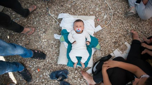 A Syrian baby lies in gravel at Kara Tepe camp, where its parents are unable to feed it. (Facebook)