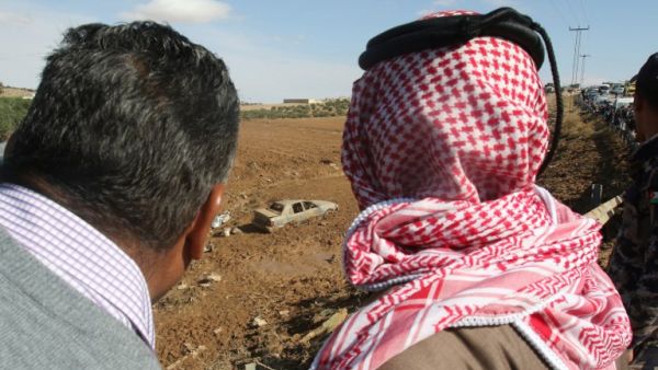 Jordanians stare at a car, submerged in mud following flash floods (AFP)