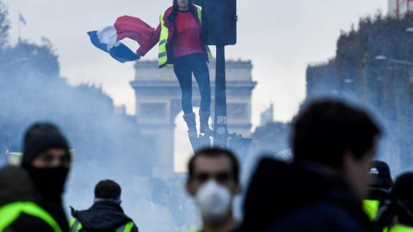 A protestor dressed in yellow vest ("gilets jaunes" in french) holds a french flag as she stands on a red light at the Champs Elysee, in Paris (AFP)