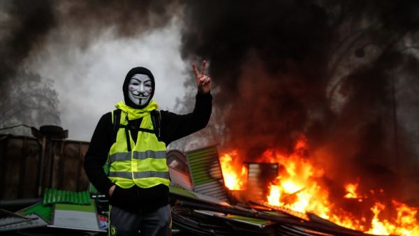 A protester wearing a Guy Fawkes mask makes the victory sign near a burning barricade during a protest of Yellow vests  (AFP)