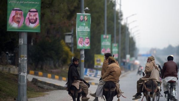 Pakistani labourers ride past welcoming posters featuring the portrait of Saudi Arabian Crown Prince Mohammed bin Salman on a street in Islamabad  (AFP)
