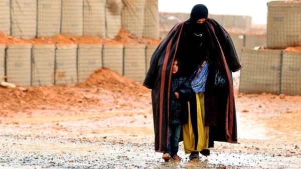 A Syrian refugee from the informal Rukban camp, which lies in no-man's land off the border between Syria and Jordan, walks in the rain on March 1, 2017. She is sheltering a young child outside a U.N.-operated medical clinic immediately on the Jordanian side (AFP/File)