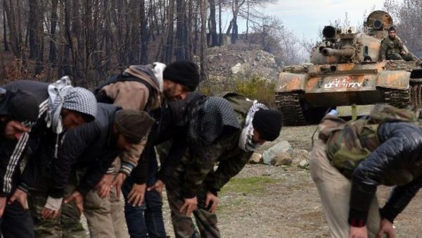 A Syrian rebel sits atop a Soviet-made T-55 tank as comrades pray on the Jabal al-Turkman mountain in Syria's northern Latakia. (AFP PHOTO/AAMIR QURESHI)