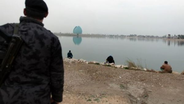 An Iraqi police officer looks at people fishing by the Tigris river facing the Shahid (martyr) Monument. (AFP PHOTO/PATRICK BAZ)