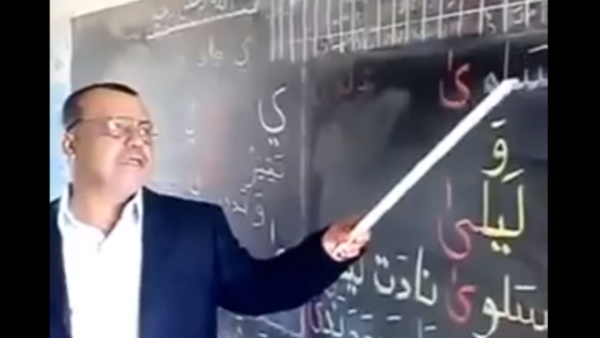 يكاد المعلم في الفيديو يرقص وهو يتغنى مع الأطفال بالحروف. 