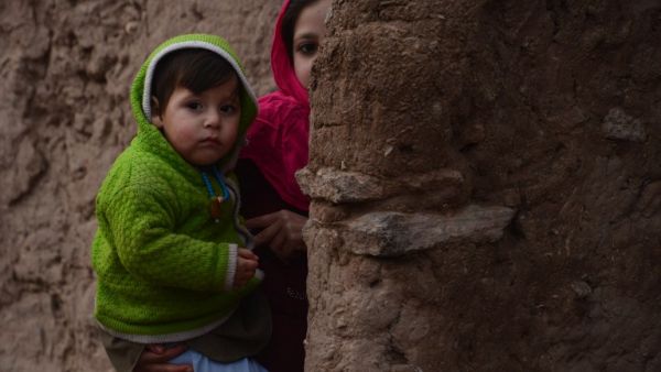 In this photograph taken on January 23, 2017, an Afghan girl holds her brother as she walks through a refugee camp in Herat. (AFP/Aref Karimi)