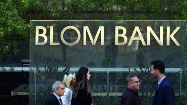 People walk past the sign of the BLOM Bank in Beirut, a day after a bomb blast hit its headquarters in Verdun. (AFP/Patrick Baz)