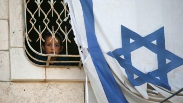 طفل ينظر عبر نافذة بيت فلسطيني يحتله مستوطنون في مدينة الخليل المحتلة والمقسمة.

