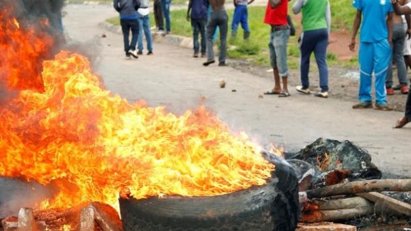 ظاهرون يقفون خلف حاجز مشتعل خلال تظاهرة على طريق مؤدية إلى العاصمة هاراري
