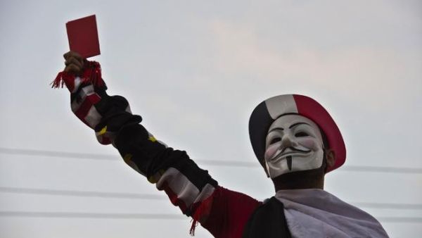A protestor wearing a Guy Fawkes mask holds up a red card as thousands of Egyptian demonstrators gather outside the presidential palace in Cairo (Khaled Desouki / AFP)